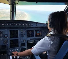 a female pilot sitting in the cockpit of an airplane looking out at the ocean and land