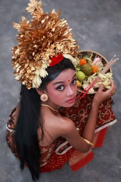 a young woman dressed in traditional thai garb holding a bowl of fruit and chopsticks