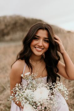 a woman in a dress holding a bouquet of flowers and smiling at the camera while standing in a field