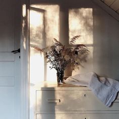 a vase with flowers sitting on top of a white dresser next to a window in a room