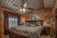 a bedroom with wooden walls and ceiling fan in the middle of the room, along with two lamps on either side of the bed