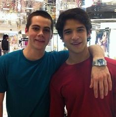 two young men standing next to each other in front of a store display with their arms around one another