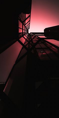 the silhouette of a building against an orange and pink sky at night, taken from below