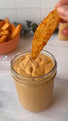 a person dipping some kind of food into a glass jar with a cracker in it