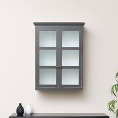 a gray cabinet sitting on top of a black table next to a potted plant