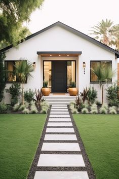 a white house with grass and plants on the front lawn, leading to an entry way