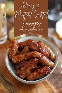 honey and mustard coated chicken wings in a bowl on a wooden table with glasses behind it