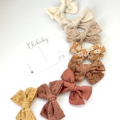 six small hair bows are lined up on a white surface with a name tag in the middle