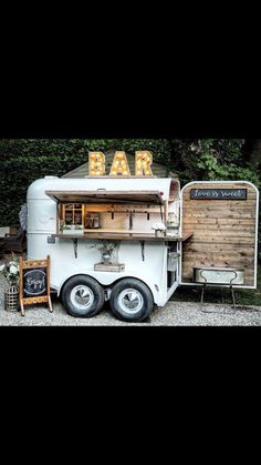 an old fashioned food truck with the word bar written on it's side and two chairs next to it