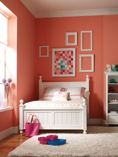 a white bed sitting next to a window in a room with orange walls and rugs