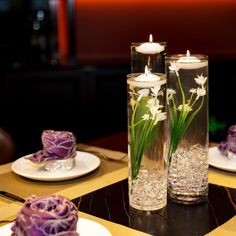 two vases with flowers in them on a table next to plates and candle holders