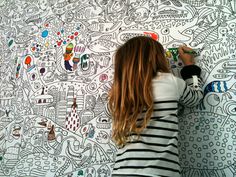 a woman writing on a wall with colorful doodles all over her body and head