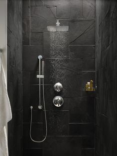 a black tiled bathroom with a shower head and hand held shower faucet in the corner