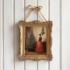 a painting hanging on the wall with a ribbon around it's edge and a christmas tree in the background