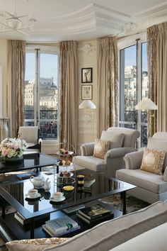 a living room filled with lots of furniture next to tall windows covered in draperies