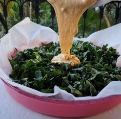 a person pouring sauce on top of greens in a pink bowl with white napkins