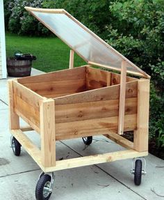 a wooden box with wheels and a glass window on the top in front of some bushes