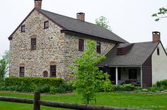 an old stone house sits in the middle of a green yard with a wooden fence