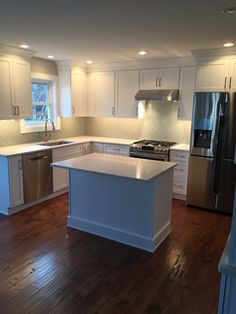 an empty kitchen with white cabinets and stainless steel appliances in the center island, along with hardwood flooring