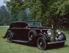 an old black car is parked in the grass