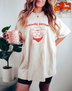 a woman holding a coffee mug and wearing a t - shirt that says meowy partner