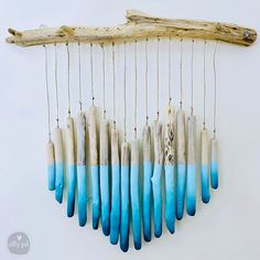 a group of blue and white beads hanging from a wooden stick on a wall next to a piece of driftwood