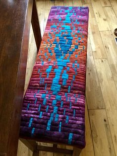 a bench with a colorful rug on top of it next to a wooden table and chair