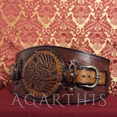 This belt is called "Threevens" from the central motif engraved on it: a triskel formed by three ravens chasing each other. This is an original design by AGARTHIS inspired by traditional Nordic arts. The belt is decorated along its length with the runic alphabet of the young Futhark. Made of genuine 3 mm thick Italian vegetable tanned leather, it is handmade and hand-dyed. Brass studs, water-repellent wax coating. Two solid brass buckles make it truly adjustable: - body: 90 cm / 35.4" - total length (with tail, adjustable): 92 - 104 cm / 36.2" - 41" - Width: 16 cm / 6.3" - Colors: light brown / dark brown / mustard Its particular design follows the shape of the hips making it truly wearable for everyone, a unisex accessory that will make your outfits special. It is recommended for your per Viking Belt, Runic Alphabet, Historical Reenactment, Brown Mustard, Nordic Art, Period Costumes, Suspender Belt, Unisex Accessories, Dec 30