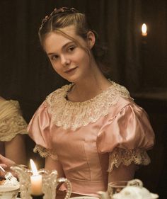 a woman sitting at a table with candles in front of her and another woman standing behind her