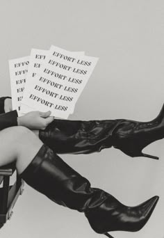 black and white photograph of woman sitting on chair with legs crossed holding papers in front of her face