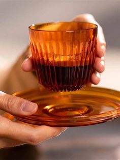 a person holding an orange glass cup and saucer