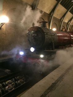 a steam engine train traveling down tracks next to a loading platform in a subway station