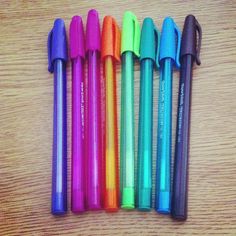 five different colored pens lined up next to each other on a wooden table with writing utensils