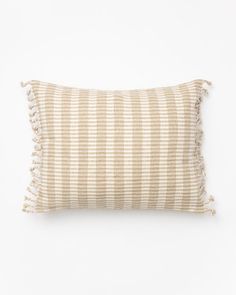 a beige and white striped pillow with tassels on the edges, sitting against a white background