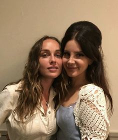 two women standing next to each other in front of a white wall and one is holding her arm around the other woman's shoulder