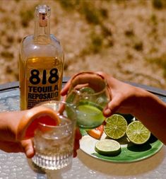 two people are holding glasses over a plate with limes