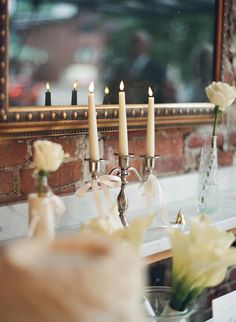 candles are lit in front of a mirror with flowers on the table next to it