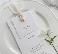 a white plate topped with a piece of paper next to a flower