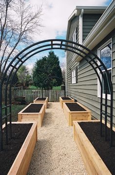 several wooden planters lined up in front of a house with gravel on the ground