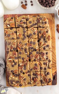 a wooden cutting board topped with brownies and pecans next to chocolate chips, eggs, and more