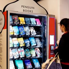 a woman standing next to a vending machine with books on it's display