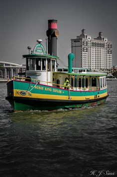 a green and yellow boat floating on top of water near tall buildings in the background