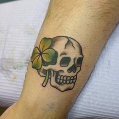 a man with a skull and clover tattoo on his arm is holding a shamrock in his hand