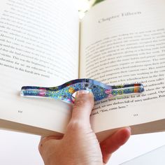 a person is holding an open book with a miniature scissors on top of it in their hand