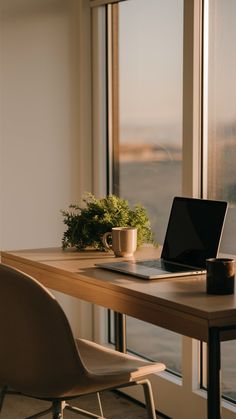 a laptop computer sitting on top of a wooden table next to a plant and cup