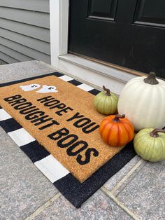 three pumpkins and two gourds are sitting on the front porch door mat