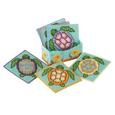 four coasters with cross stitch designs on the front and back, each decorated in different colors