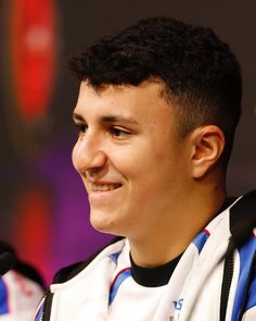 a smiling young man wearing a white and blue jacket sitting in front of a microphone