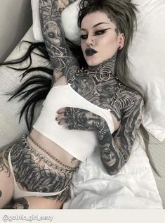 a woman laying in bed with tattoos on her body