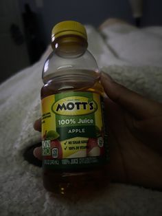 a hand holding a bottle of mott's juice on top of a bed